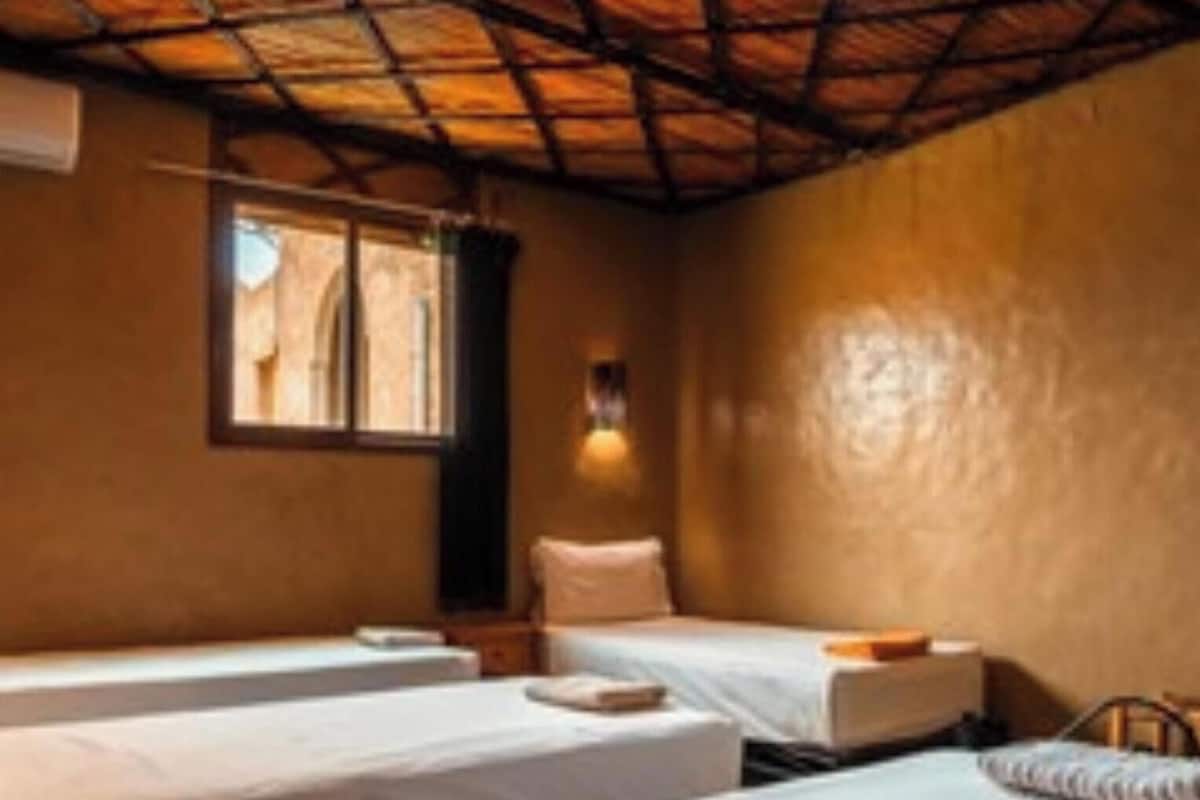 A room with two single beds, a window with curtains, and a wall-mounted light fixture.
