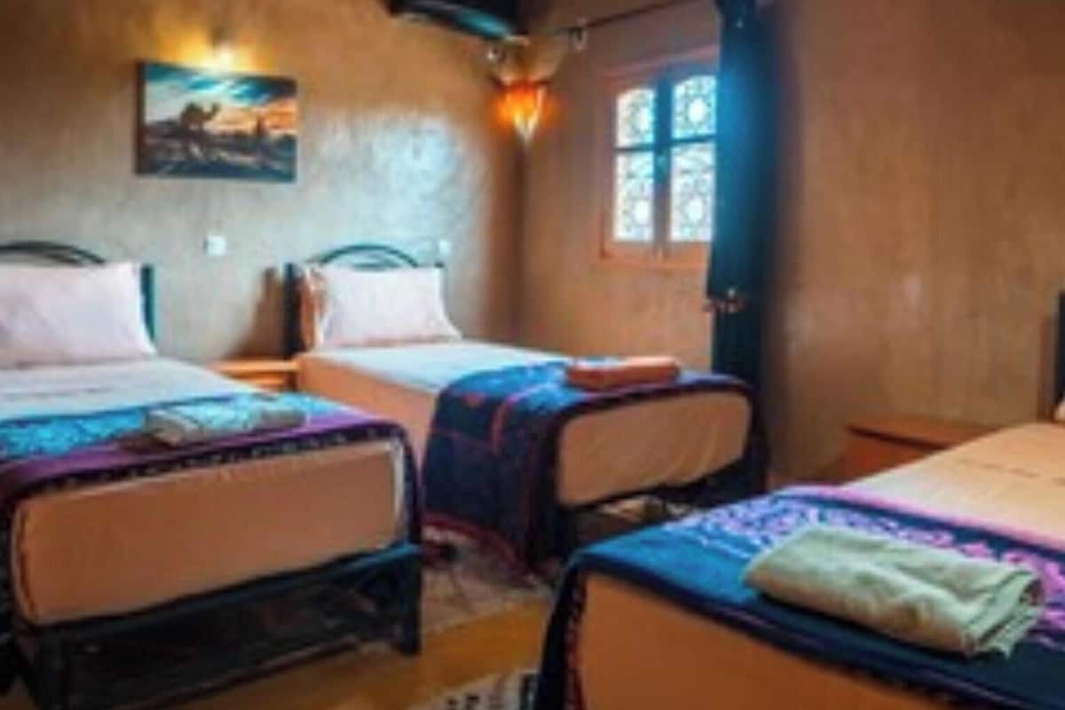 A room with two beds, a painting on the wall, and a window with curtains.