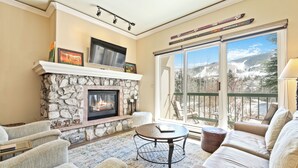 A living room with a stone fireplace, a television, and a balcony with a ski rack. - Beaver Creek Ski-In/Ski-Out Retreat  LB108 (Beaver Creek)