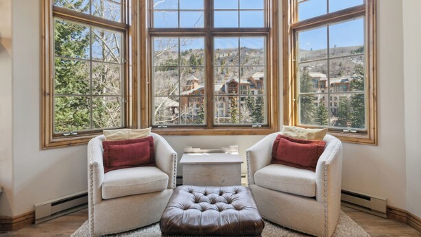 A corner room with large windows, a white sofa, a brown ottoman, and a small table. - Ski-In/Ski-Out, Resort Amenities, Shuttle | LB113 (Beaver Creek)