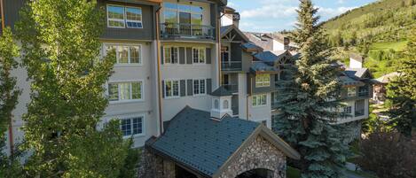 A multi-story hotel with a stone entrance, large windows, and a view of a mountainous landscape.