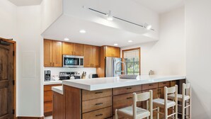 Una cocina moderna con armarios de madera, una isla grande con taburetes de bar, electrodomésticos de acero inoxidable y un ventanal que proporciona luz natural.