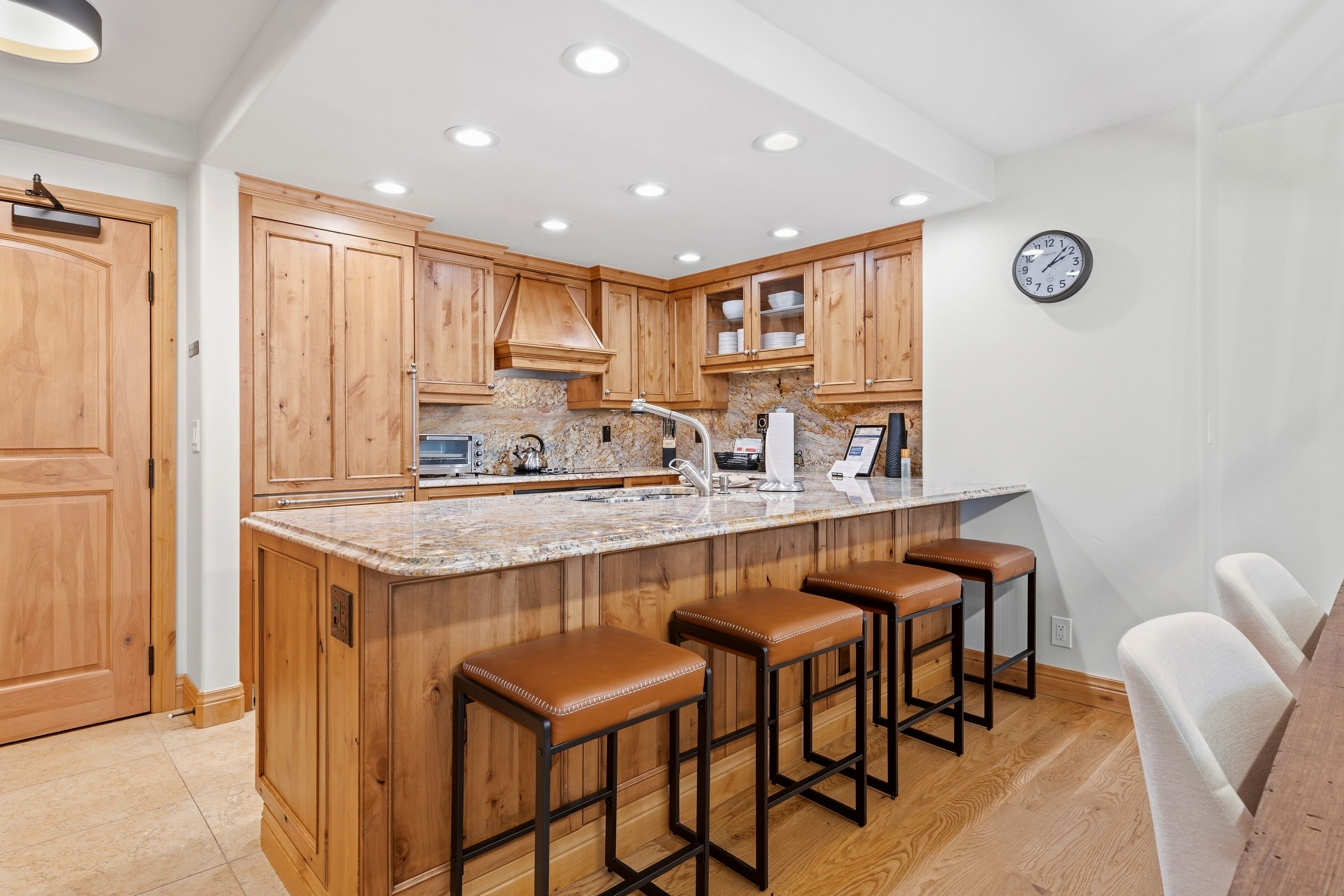 A kitchen with wooden cabinets, a granite countertop, a built-in stove, and a clock on the wall.