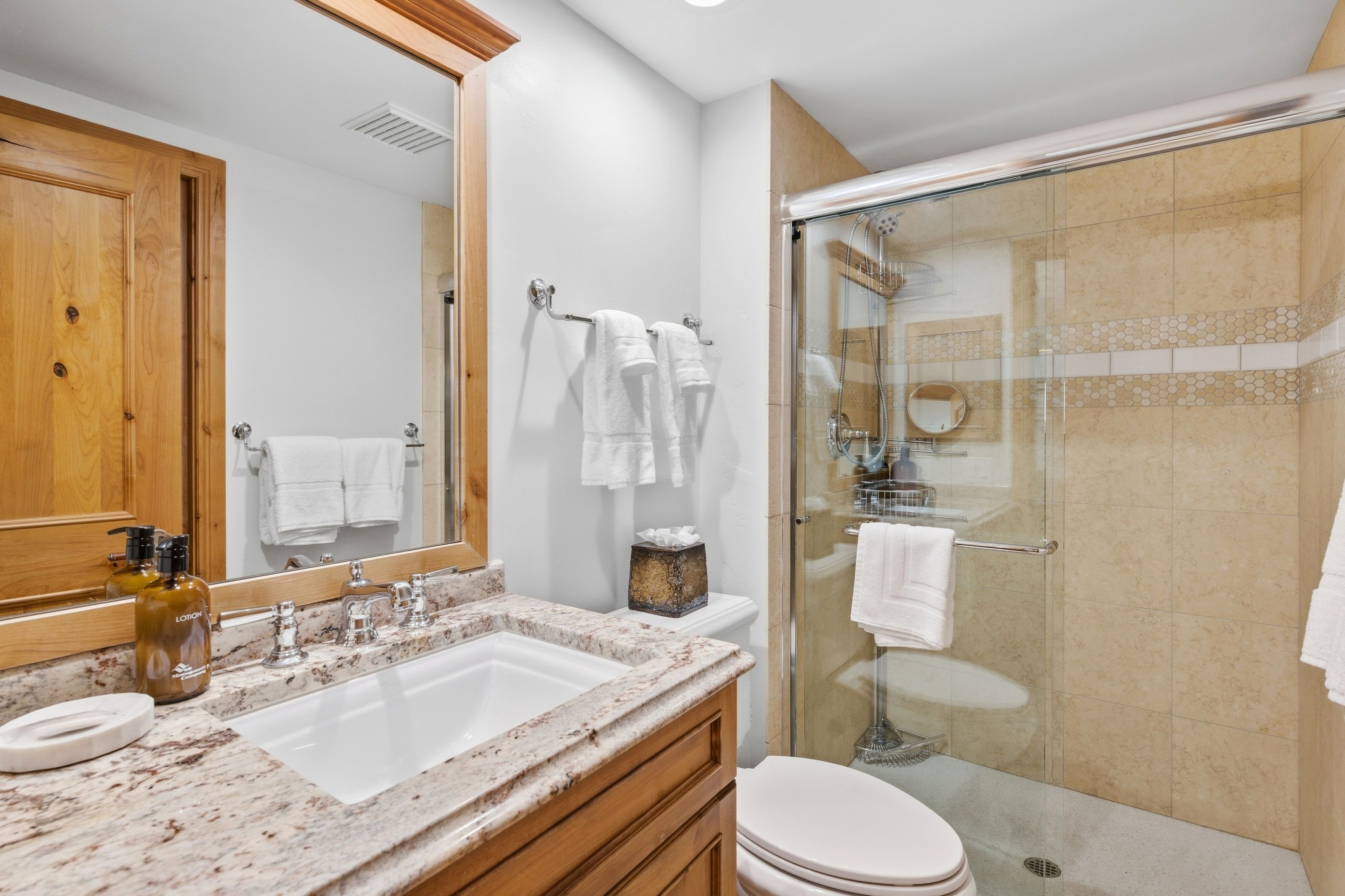 Une salle de bain avec un lavabo en marbre, un grand miroir, une douche en verre et plusieurs serviettes blanches.