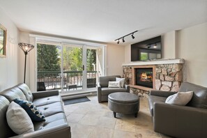 Ein Wohnzimmer mit Kamin, Ledersofas und einer großen Schiebeglastür, die auf eine Terrasse im Freien führt.