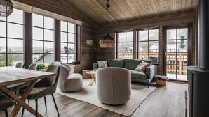 Un vaste espace de vie doté d’un plafond en bois, de grandes fenêtres, d’un canapé vert, d’un pouf rond et d’une table à manger avec des chaises.