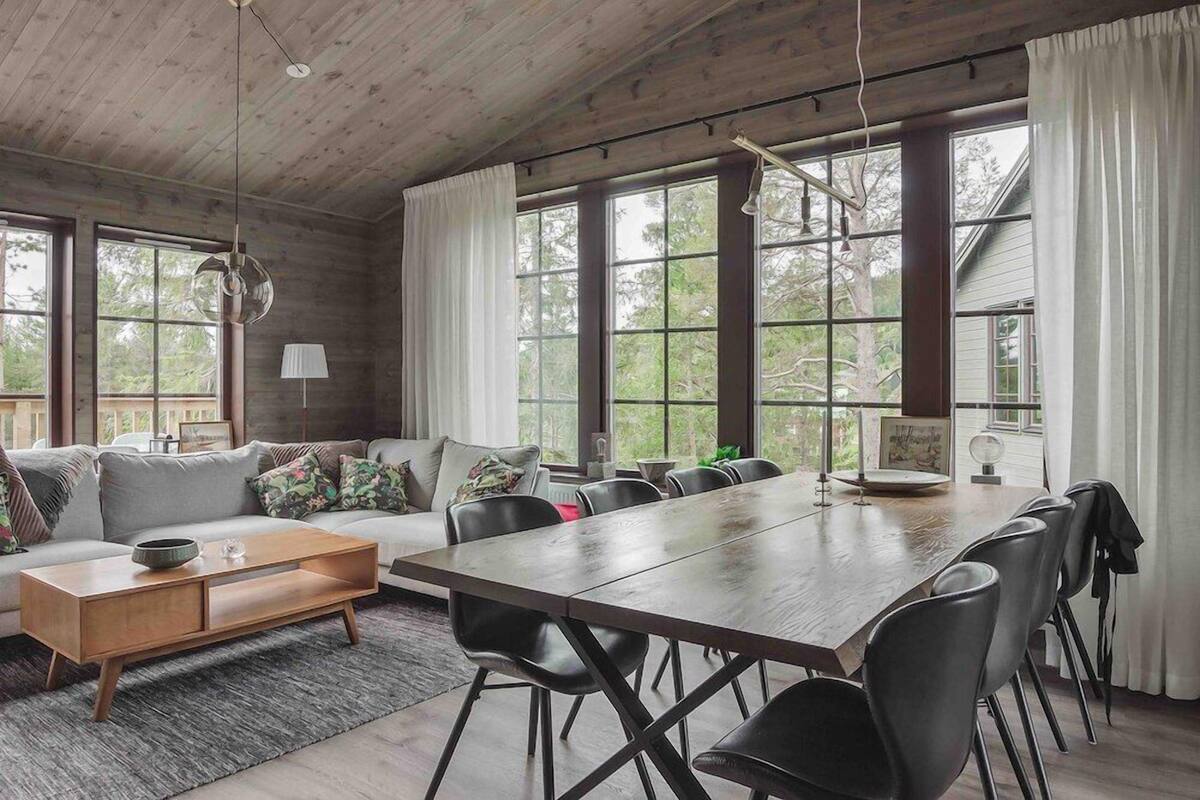 Una habitación amplia con techo de madera, ventanas grandes, un sofá, una mesa de comedor y sillas.