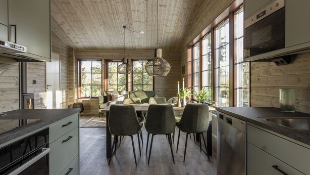 Une cuisine moderne avec un plafond en bois, de grandes fenêtres et un coin repas comprenant des chaises et une table.