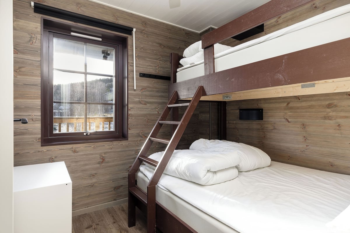 Habitación con literas, ventana, paredes de madera y una escalera.