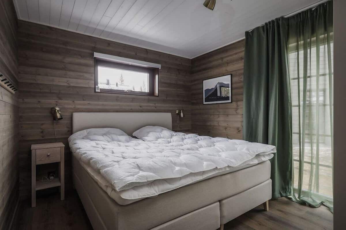 Un dormitorio con cama, mesita de noche, ventana y un cuadro en la pared.