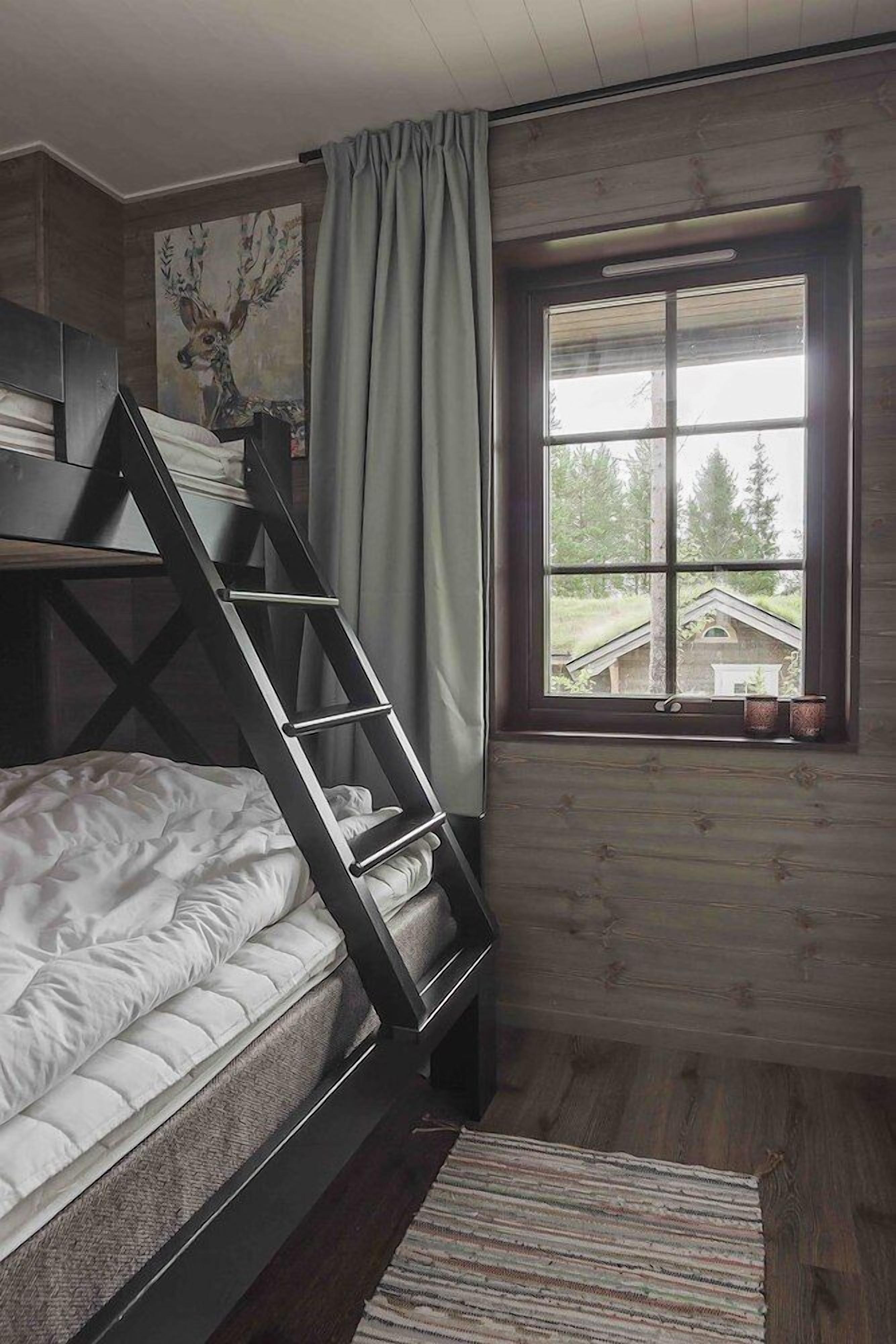 Una habitació amb un llit superposat, una finestra amb vistes, una escala i un quadre a la paret.