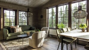L’intérieur d’un chalet accueillant, avec un canapé, des fauteuils, une table à manger et de grandes fenêtres donnant sur la forêt.