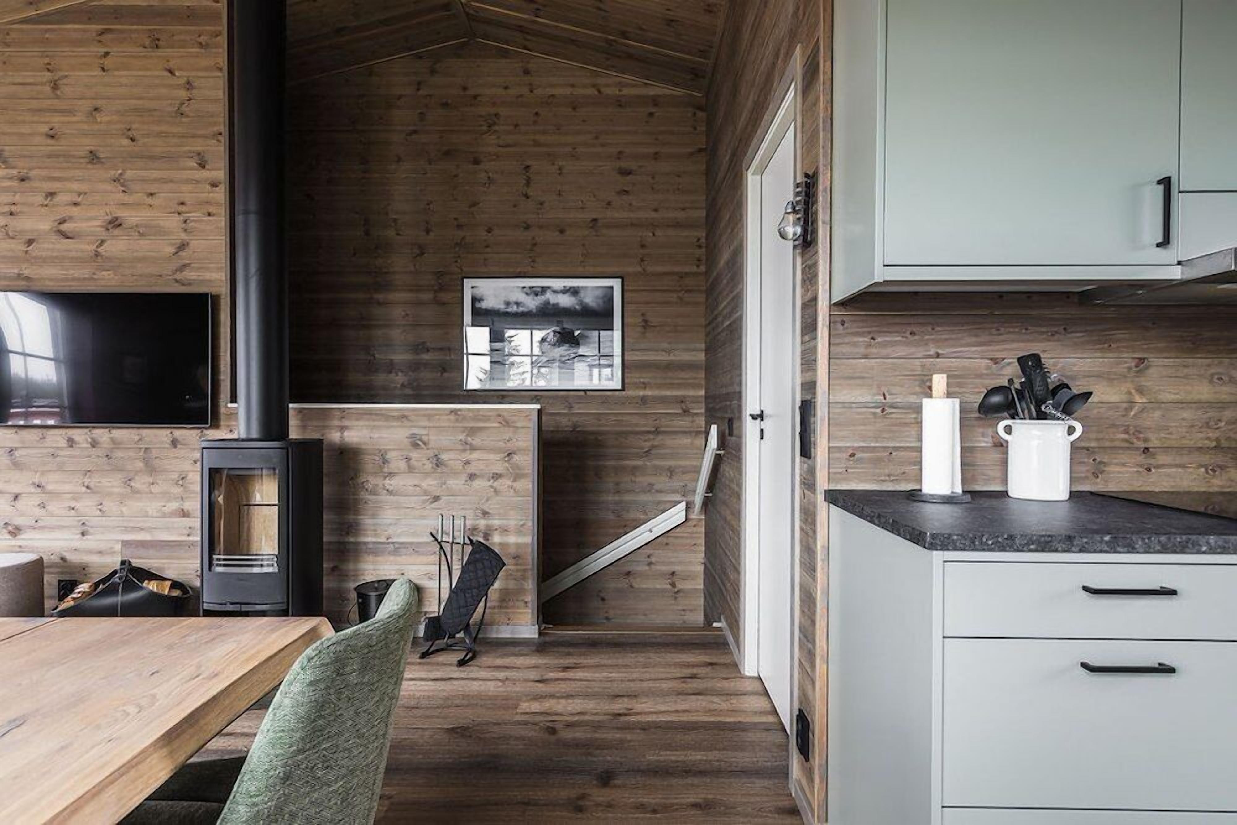 Acogedor interior de cabaña con detalles de madera, chimenea, comedor y cocina con alacenas y encimera.