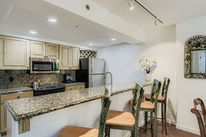 Eine Küche mit Granit-Arbeitsplatten, Edelstahlgeräten, Holzstühlen und einem dekorativen Spiegel.