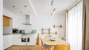 Una cocina moderna con una isla central, una zona de comedor con mesa y sillas de madera, y vistas al exterior a través de grandes ventanales.