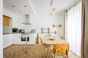 Eine moderne Küche mit einer zentralen Kochinsel, einem Essbereich mit Holztisch und Stühlen sowie Blick ins Freie durch große Fenster.