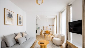 Un salón moderno con un sofá gris, una mesa de centro redonda de madera, un sillón blanco y un televisor de pantalla plana.