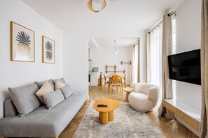 Ein modernes Wohnzimmer mit einer grauen Couch, einem runden Holztisch, einem weißen Sessel und einem Flachbildfernseher.
