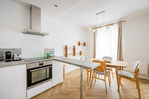 Eine moderne Küche mit Einbauofen, einem Essbereich mit Holztisch und Stühlen sowie einem großen Fenster mit Vorhängen.