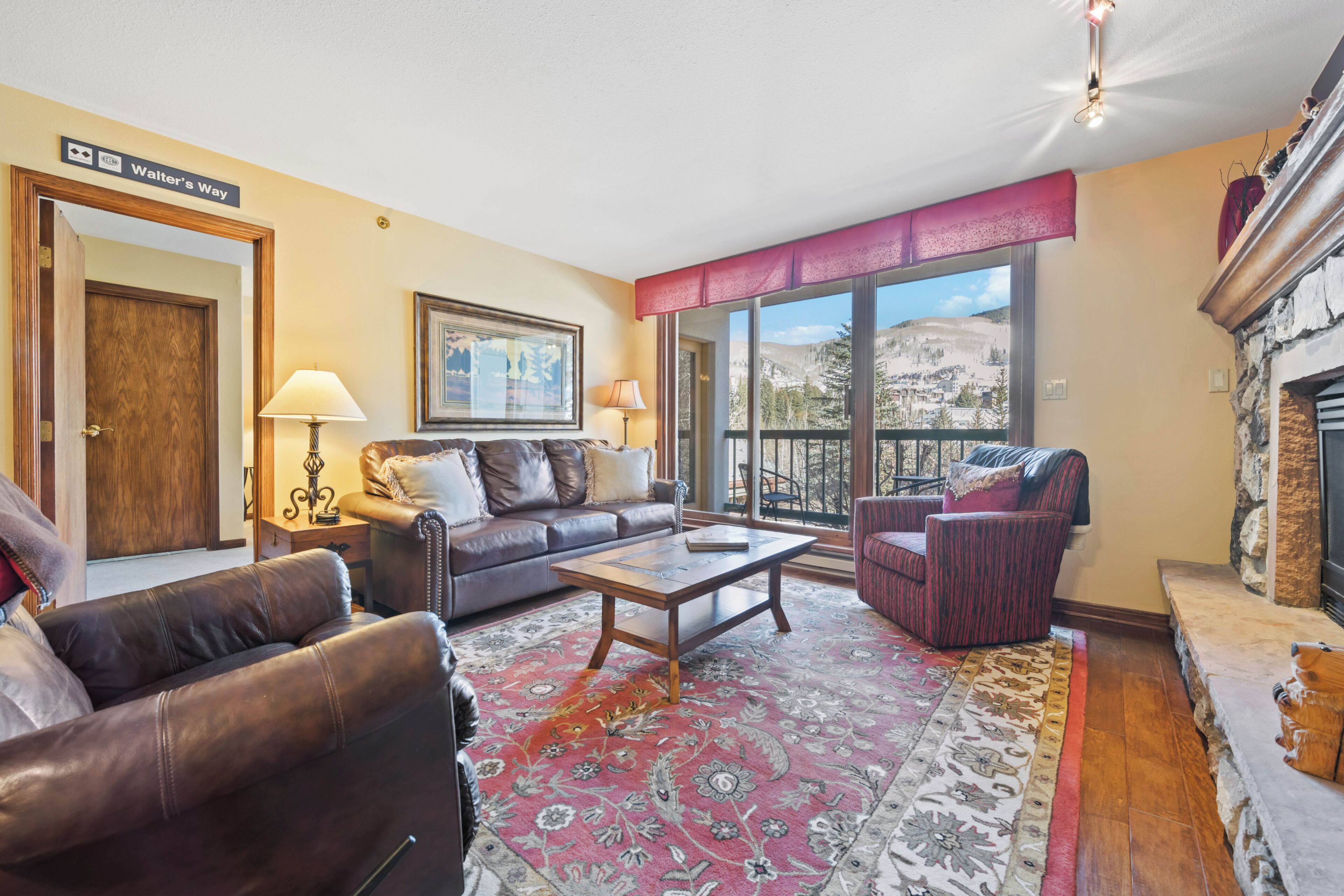 A living room with leather sofas, a coffee table, a fireplace, and a large window with a mountain view.