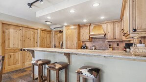 Una cocina con armarios de madera, encimera de mármol y dos taburetes.