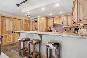 A kitchen with wooden cabinets, a marble countertop, and two stools. - Ski-In/Ski-Out, Pool, Hot Tubs, Fitness Room | LB208 (Beaver Creek)