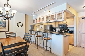 Eine Küche mit Barbereich, Holzschränken, einem Kühlschrank und einer Wanduhr.