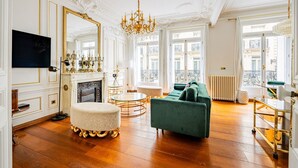 A room with a fireplace, a green sofa, a round table, and a chandelier. - Champs Elysées-Avenue Montaigne-2 rooms (Paris)
