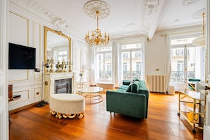 Ein Zimmer mit Kamin, einem grünen Sofa, einem runden Tisch und einer Kronleuchter.