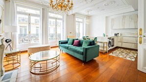 A spacious living room with a green sofa, a glass coffee table, and a chandelier. - Champs Elysées-Avenue Montaigne-2 rooms (Paris)