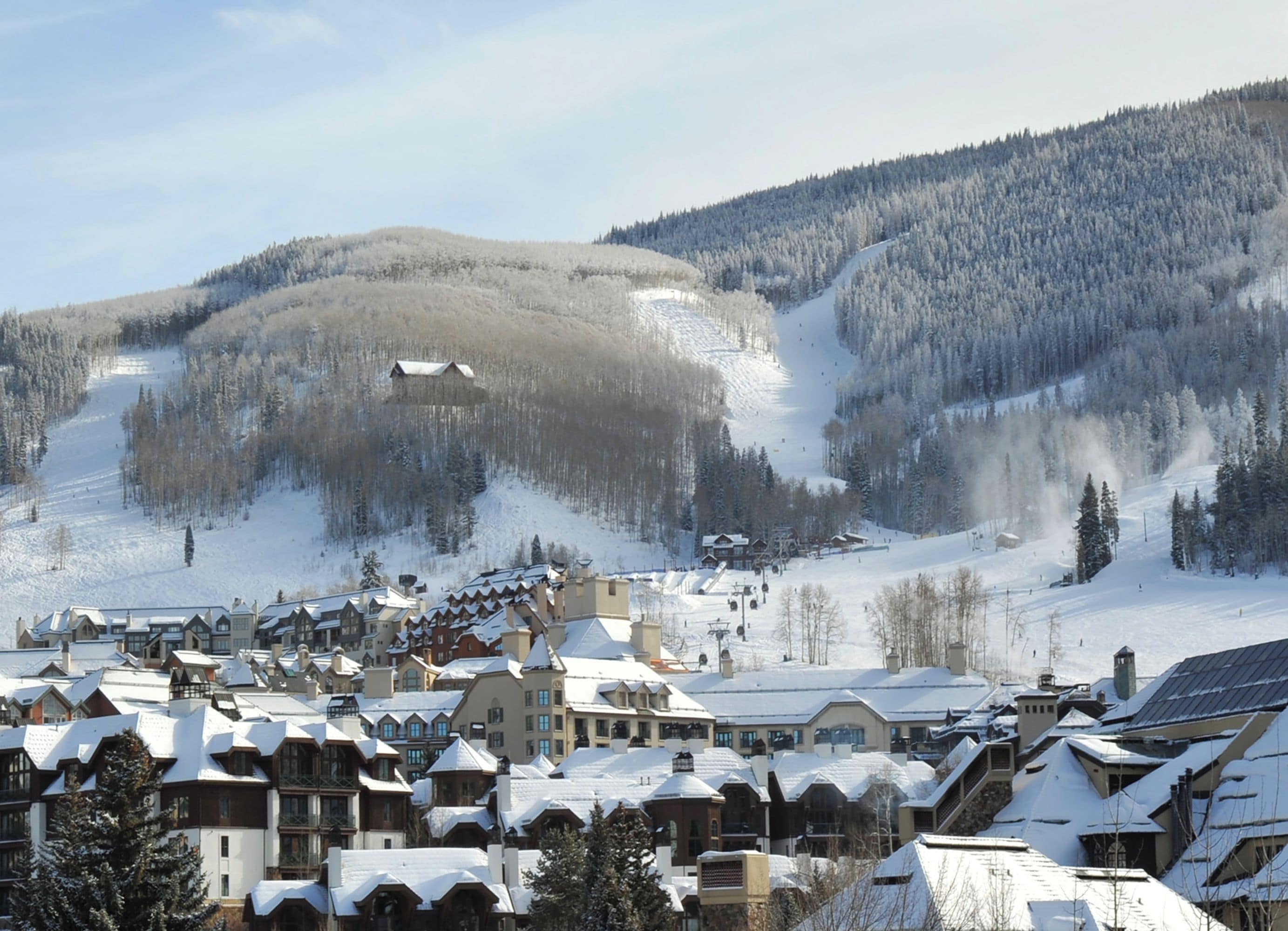 A snow-covered mountain town with traditional chalet-style buildings, a ski slope, and a clear sky.