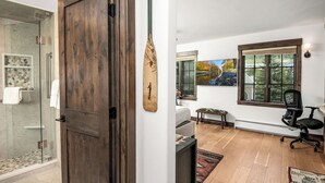 Ein modernes Interieur mit Holztür, Glasdusche, einem Gemälde, einer Bank und einem Schreibtisch.