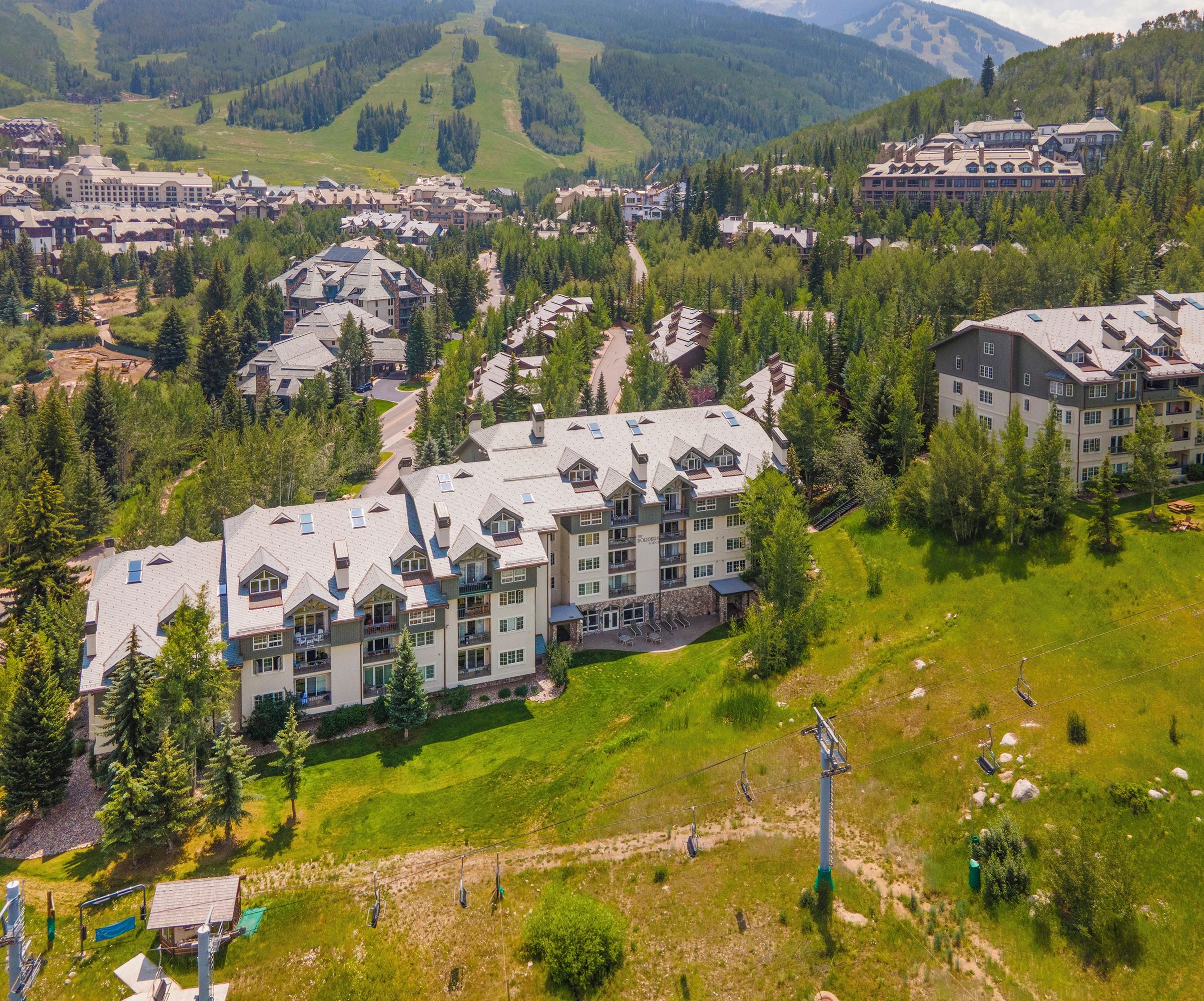 A large resort with multiple buildings, a ski lift, and a mountainous backdrop.