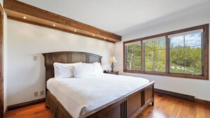 A bedroom with a large bed, wooden headboard, a nightstand with a lamp, and a large window with a view of trees. - Luxury Amenities, Beaver Creek Ski-In/Ski-Out | LB303   2 Bedroom condo (Beaver Creek)