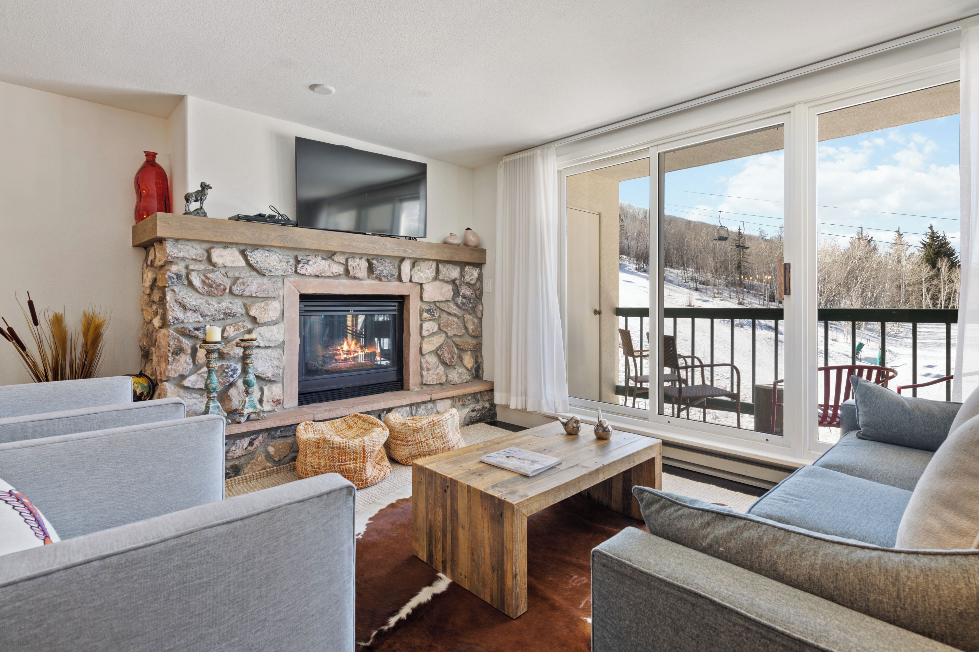 A living room with a stone fireplace, a television, and a large window with a view of a snowy landscape.