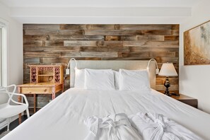 A hotel room with a wooden headboard, a bed with white linens, a desk with a chair, a nightstand with a lamp, and a painting on the wall. - Beaver Creek Ski-In/Ski-Out w/Amenities | LB305   2 Bedroom (Beaver Creek)