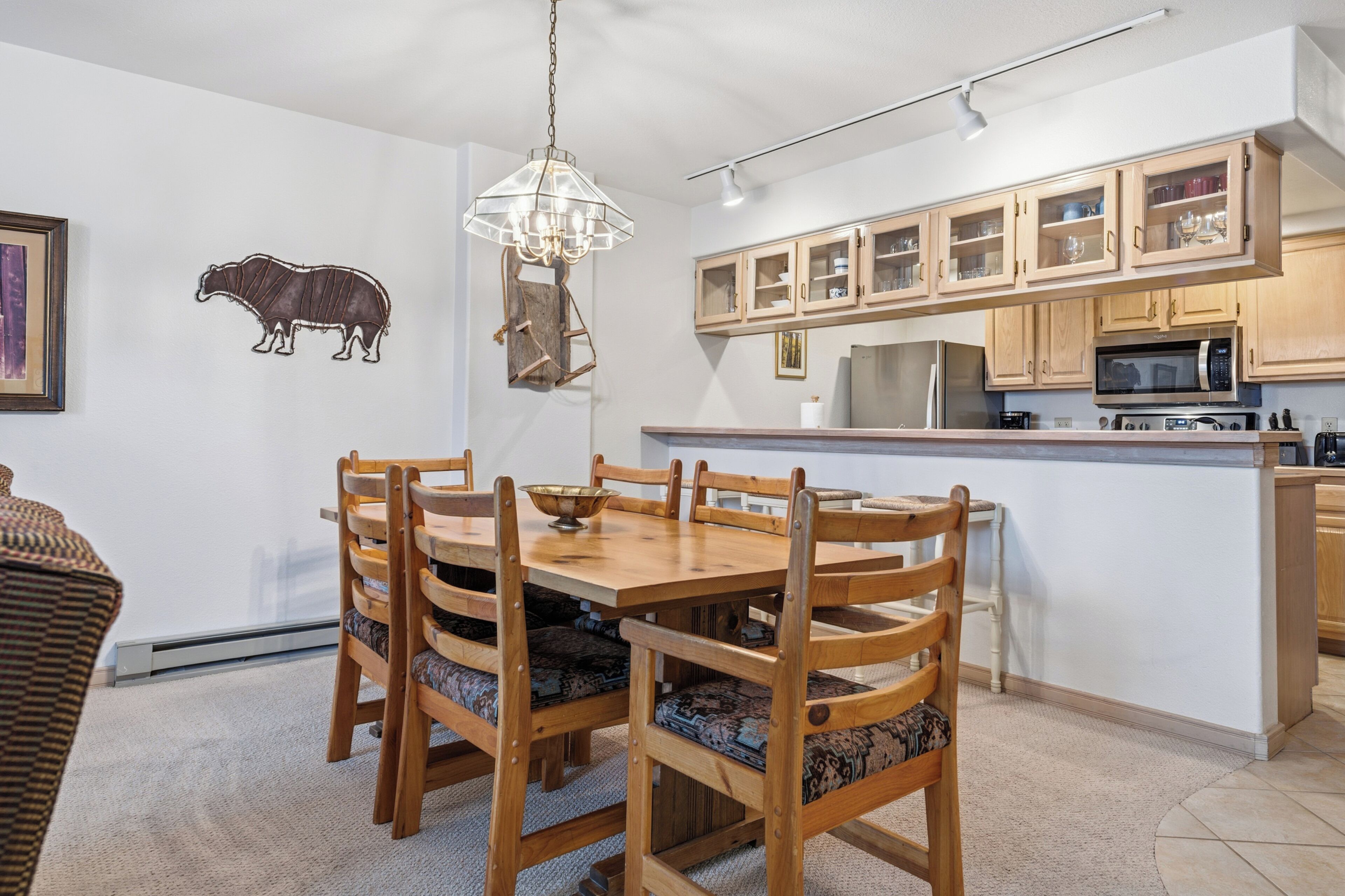 Un comedor con mesa y sillas de madera, una araña y una cocina con armarios y electrodomésticos de madera.