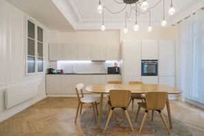 A modern kitchen with white cabinetry, a dining table with chairs, and a chandelier. - Champs Elysées!Montaigne, New&Luxurious 6pers flat (Paris)