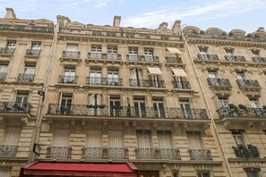 A multi-story building with balconies, large windows, and a red awning at the ground level. - Champs Elysées!Montaigne, New&Luxurious 6pers flat (Paris)