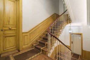 A wooden staircase with a handrail, carpeted steps, and a door at the bottom. - Champs Elysées!Montaigne, New&Luxurious 6pers flat (Paris)
