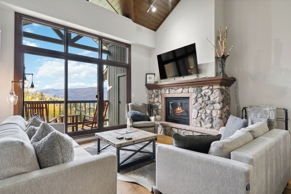 A spacious living room with a stone fireplace, comfortable seating, a flat-screen TV, and a large sliding glass door leading to an outdoor area. - Ski-In/Ski-Out, Resort Amenities, Shuttle | LB309  3 Bedroom (Beaver Creek)