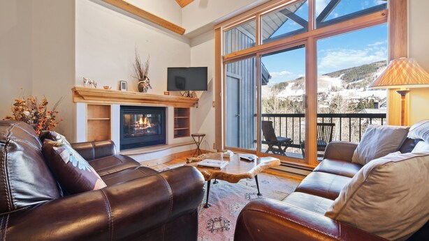 Una sala de estar con sofás de cuero, chimenea, televisión y un ventanal con vistas a un paisaje nevado.