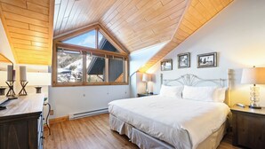 Un dormitorio con una cama grande, techo de madera, tragaluz y vistas a un paisaje nevado.