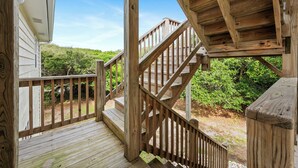 Una terraza de madera con una escalera que conduce a un espacio cubierto, rodeada de vegetación.