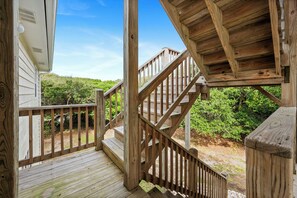 Eine Holzterrasse mit Treppe zu einem überdachten Bereich, umgeben von viel Grün.