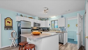 Una cocina con una isla central, armarios blancos, un refrigerador y un microondas.