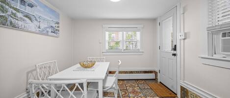 Ein Zimmer mit Esstisch, Stühlen, einem Gemälde, einem Fenster und einem Musterfußboden.