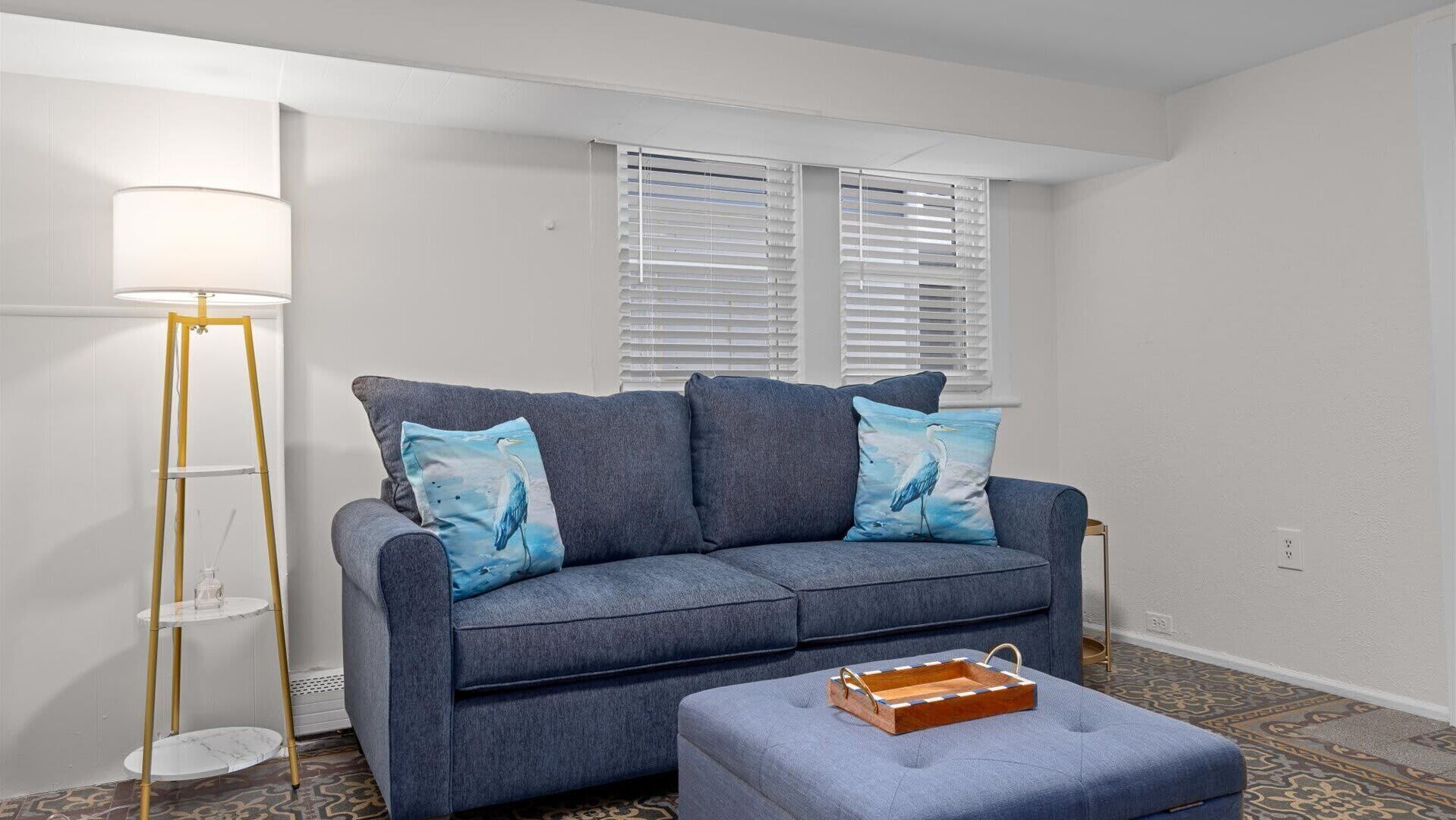 A living room with a gray sofa, two pillows with bird designs, a floor lamp, and a small wooden side table.