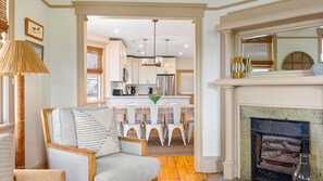 A living room with a fireplace, a dining area with a chandelier, and a kitchen in the background.