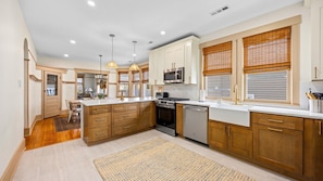 A modern kitchen with wooden cabinets, a central island, stainless steel appliances, and large windows with blinds.